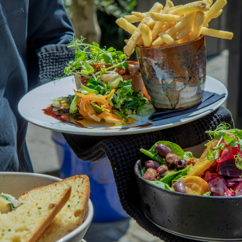 Waiter carrying a plate of food at The Three Horseshoes Inn, a pub in Lickfold near Goodwood and Cowdray Estate